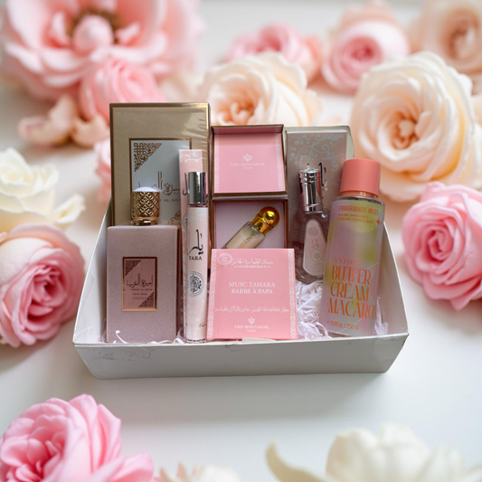 Coffret parfumé élégant sur fond blanc, entouré de roses rose poudré et blanc nacré, avec parfums et brumes florales délicates. 